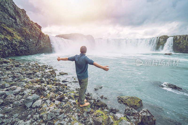 年轻男子伸开双臂望着冰岛壮观的瀑布