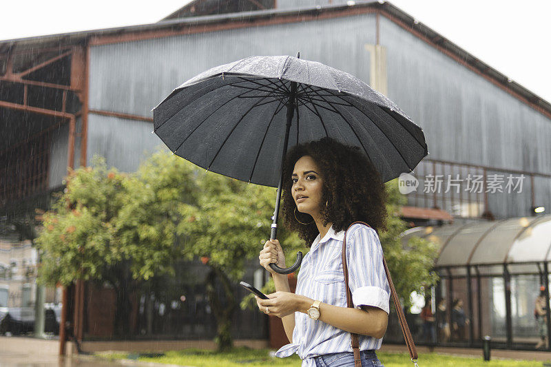 一名年轻女子在雨天用智能手机等出租车