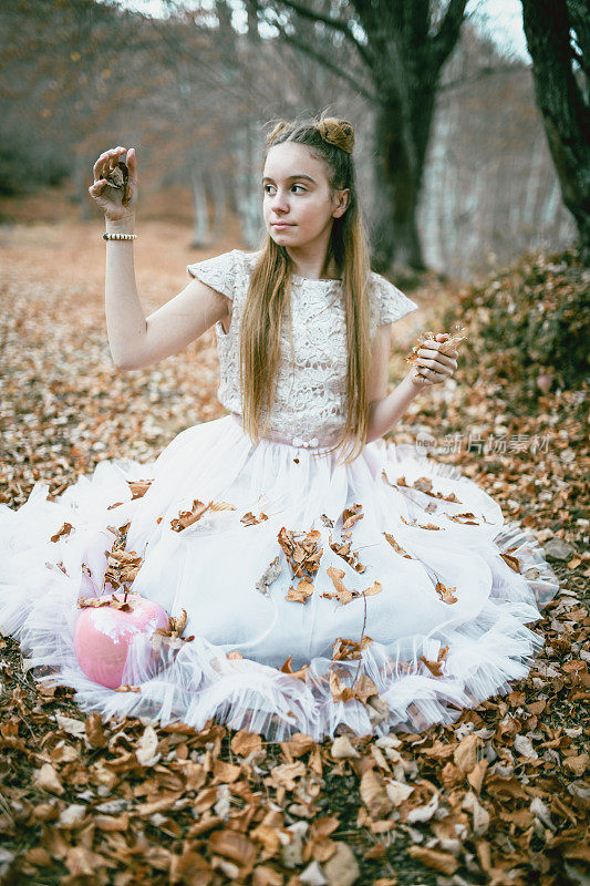 可爱的小女孩坐在落叶上，穿着白色的裙子