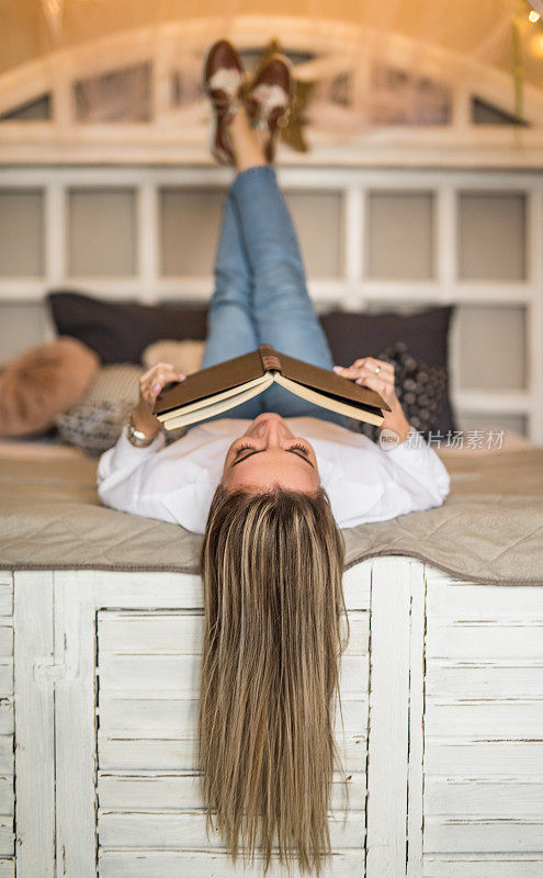 顽皮的年轻女子躺在床上，一边读书一边做白日梦。