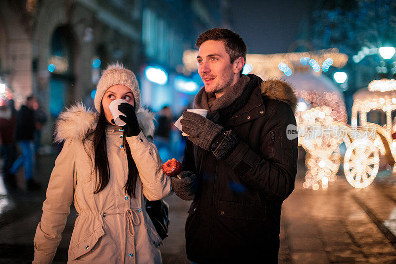 年轻夫妇在为圣诞节装饰的街道上喝着热饮