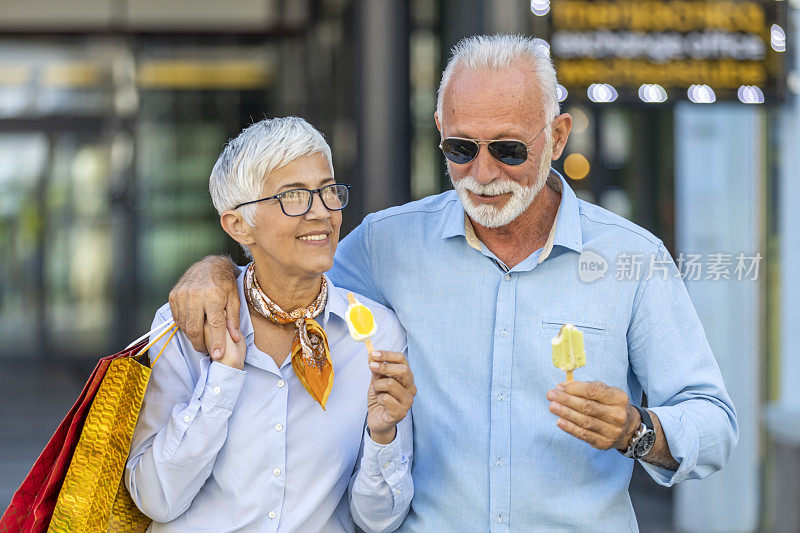 一对时尚的老夫妇在逛完购物中心后正在城市的街道上吃冰淇淋