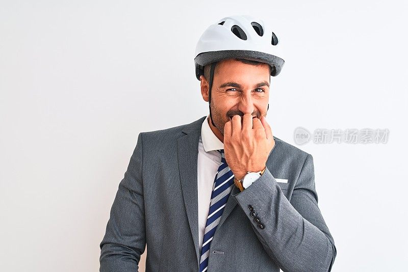 年轻英俊的商人穿着西装和领带和自行车头盔在孤立的背景看起来紧张和紧张的手在嘴咬指甲。焦虑的问题。
