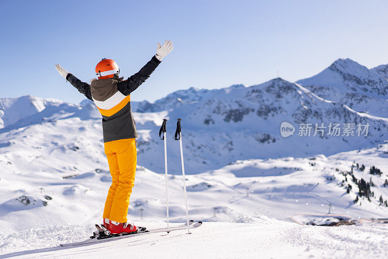 滑雪女子张开双臂，在山上享受阳光明媚的滑雪日