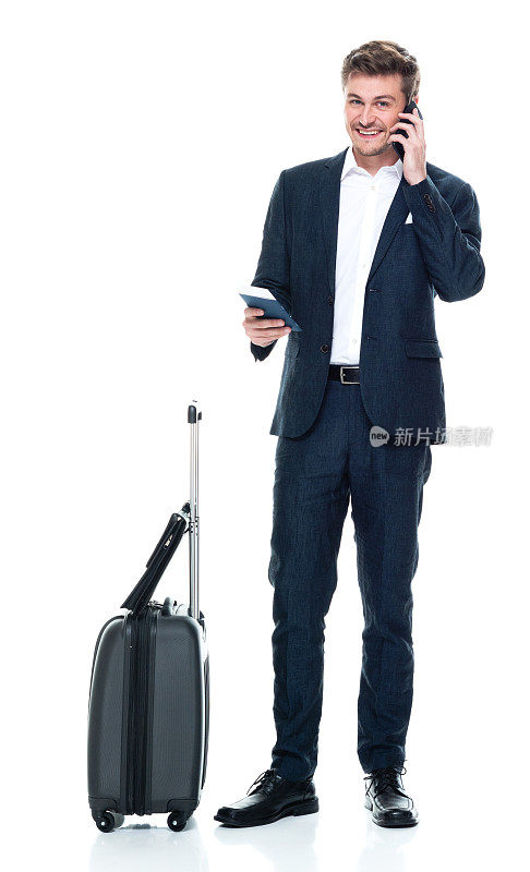 白人男性商人穿着商务装站在白色背景前，拿着行李，使用手机
