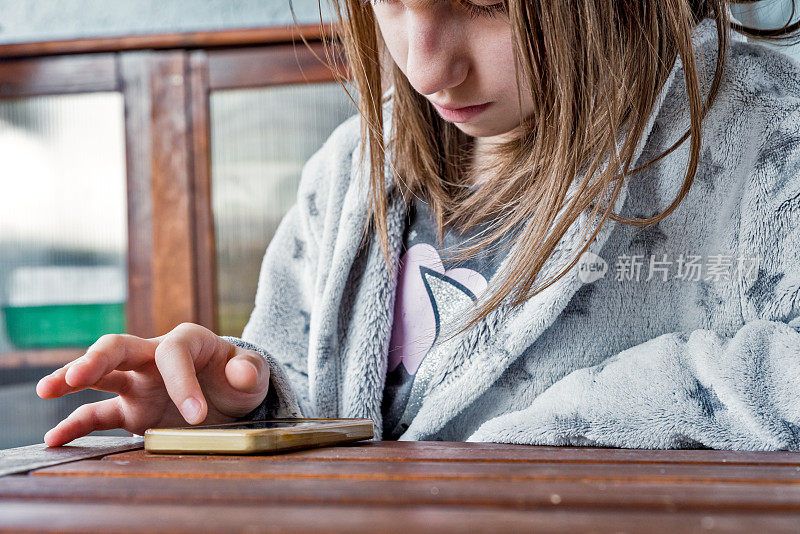 女孩在家中被隔离，穿着蓬松的灰色晨衣看手机