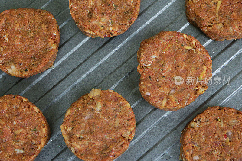 一排排自制的生牛肉饼，在厨房的工作台上烤盘准备在烤箱中烹饪