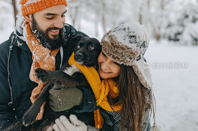 一对夫妇在雪中与狗玩耍