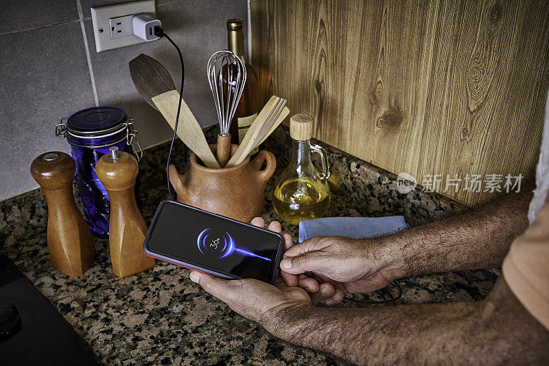 在家庭厨房里，一名男子用手将充电电缆连接到智能手机上