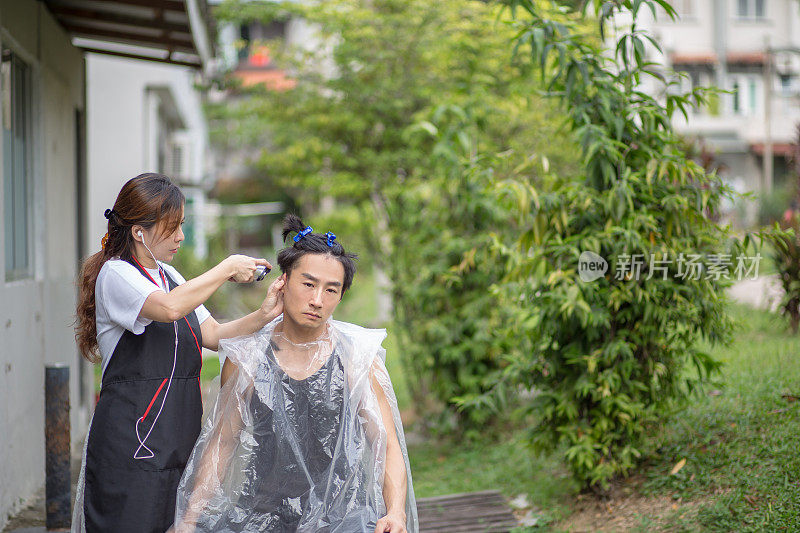 一位亚洲华人妻子在家里帮丈夫剪头发，因为疫情不能去理发店。