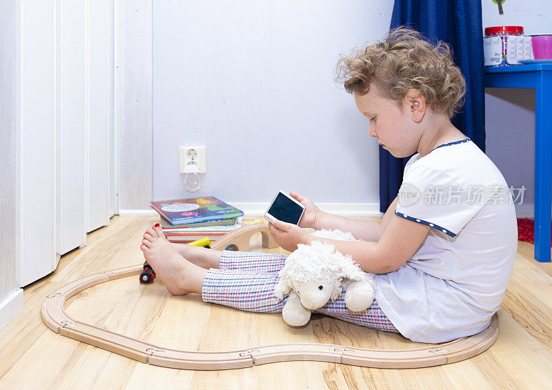 6岁的白人女孩，坐在地板上用手机进行视频交流。在线培训。