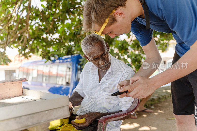 斯里兰卡加勒，一名年轻游客用智能手机上的GPS向街头小贩问路