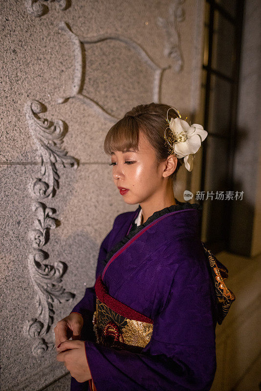 年轻女子的肖像在“Furisode”和服站在白色墙壁在晚上