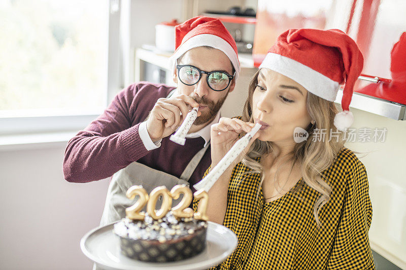 年轻夫妇在家里玩吹喇叭，用点燃的2021蜡烛制作并装饰巧克力蛋糕