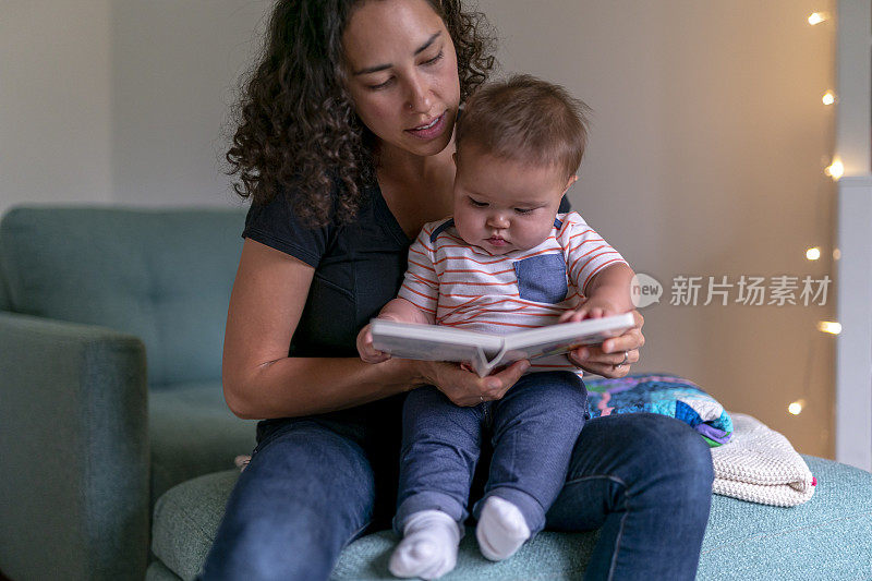 年轻慈爱的母亲给可爱的宝宝读睡前故事书