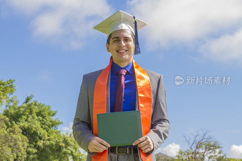 快乐幸福的肖像英俊的拉丁男学生穿着长袍和帽子，出席他的毕业典礼在美国