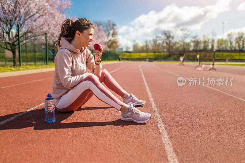 运动的年轻女子在跑道上跑步后吃苹果。