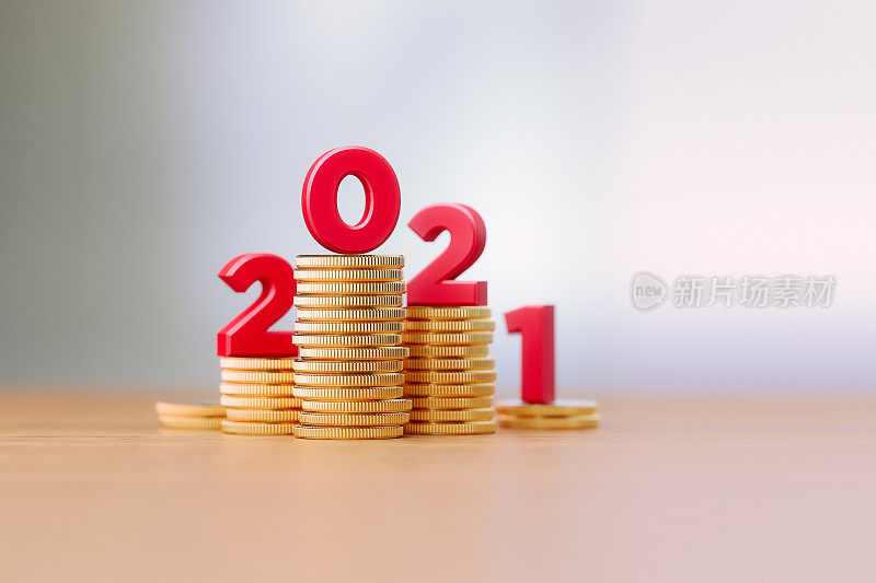 坐在硬币堆上的红色字母在背景散焦前写2021