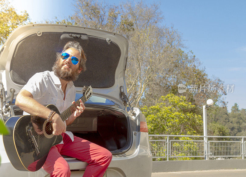 英俊的嬉皮士弹着吉他，在他的车里享受着阳光灿烂的一天