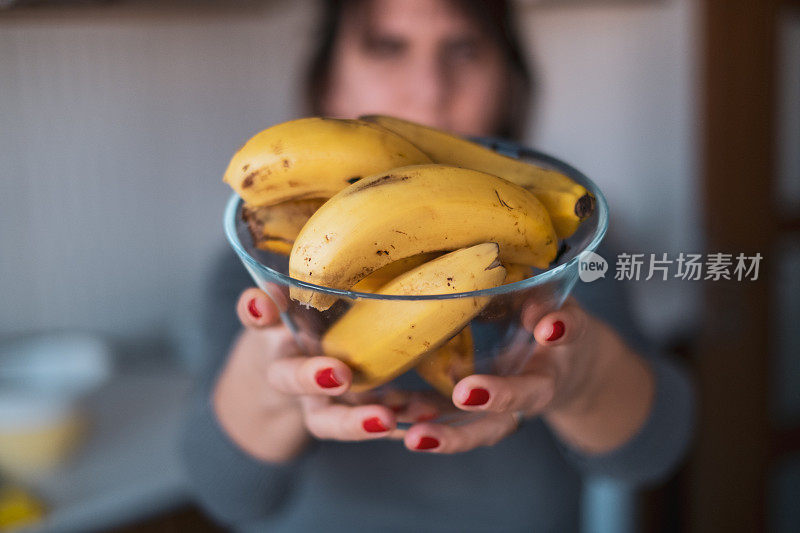 拿着一个装满香蕉的碗对着镜头的女人