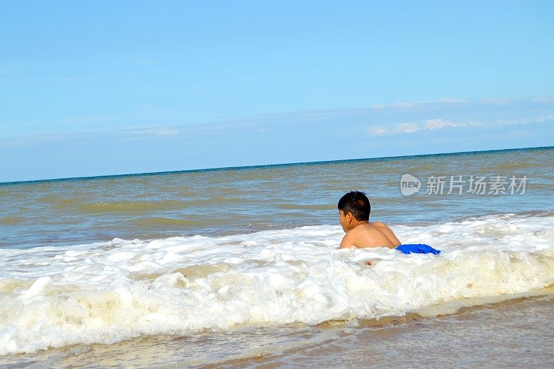 一个十岁的男孩弯下腰躺在海滩上的汹涌的海浪中