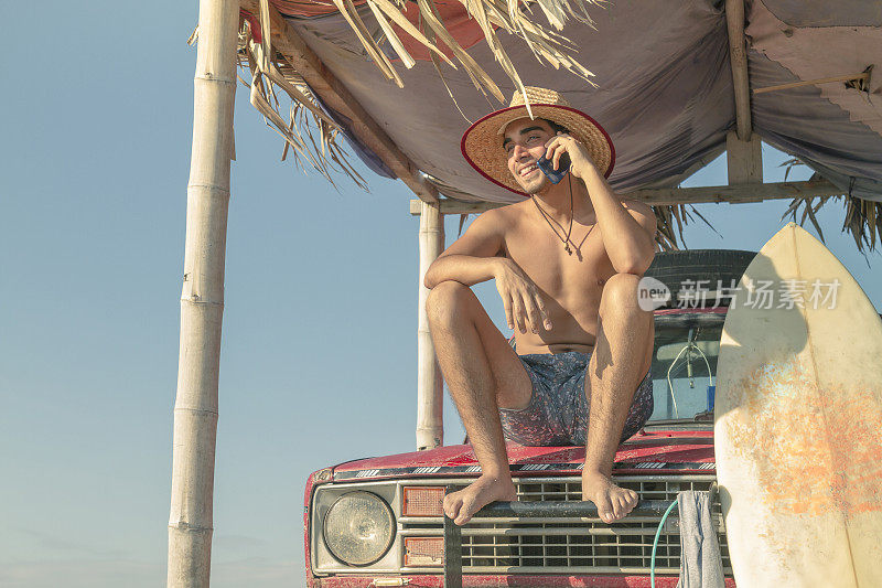在拉丁美洲厄瓜多尔瓜亚斯省的普拉亚斯，一位拉丁健康男子一边打电话一边冲浪