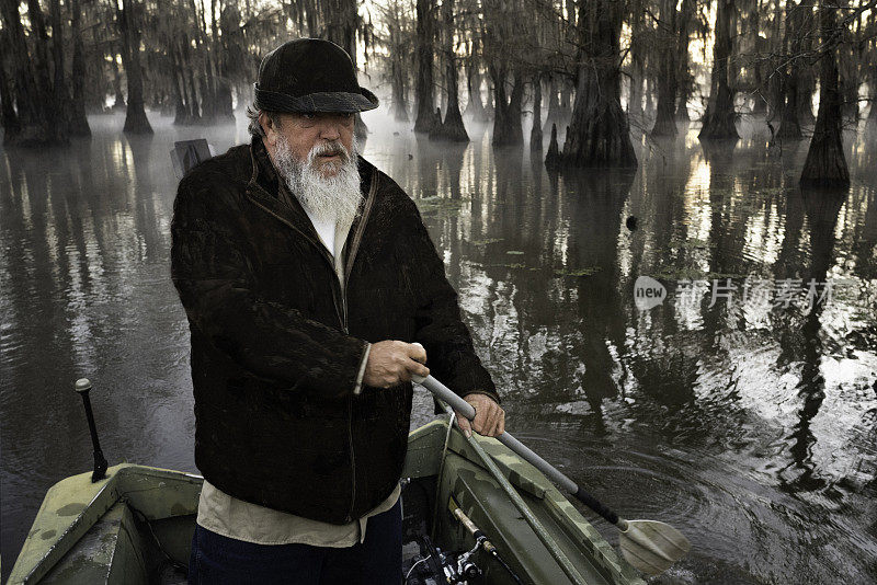 一名男子划着他的船穿过一个浅的光秃秃的柏树沼泽，卡多湖，在路易斯安那州和德克萨斯州之间的边界，美国