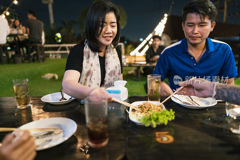 一群年轻的亚洲朋友聚会，喝啤酒，吃泰国菜在户外餐厅