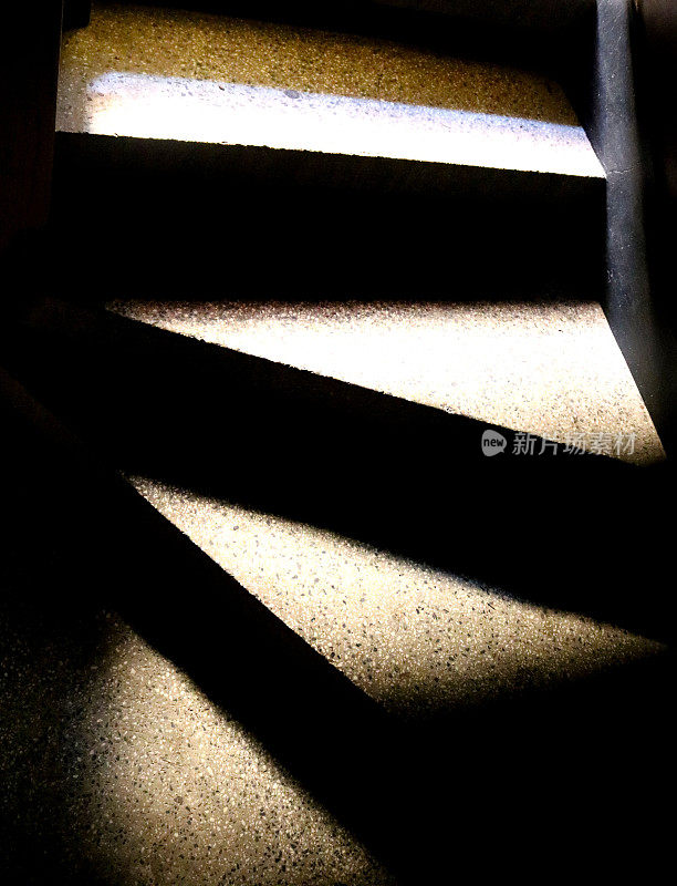 狭窄的三角形楼梯台阶位于黑暗的地方，表面有强烈的金色照明，创造了一种对比和神秘感