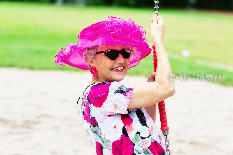 操场上的秋千上，古怪的老妇人戴着粉红色的帽子，穿着花卉图案的衣服