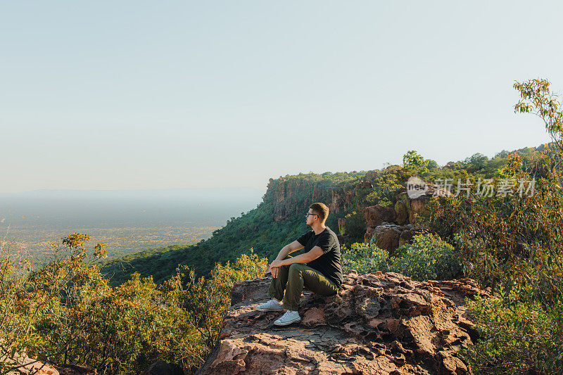 一名男性旅行者在纳米比亚的山顶上凝视着日落美景