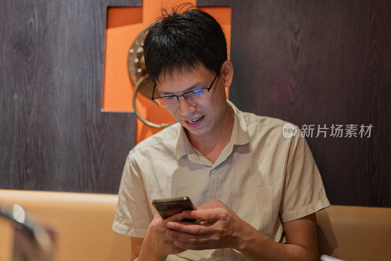 亚洲男子在餐厅座位上使用智能手机