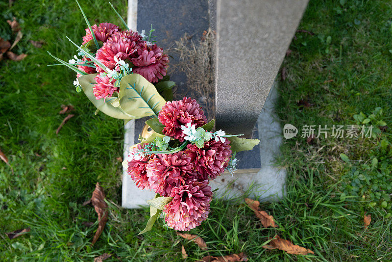 一束古老的红色人造花，插在大墓碑旁的铜花瓶里。