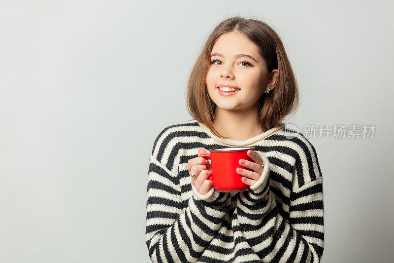 美丽的女孩在条纹毛衣与红色马克杯在白色背景