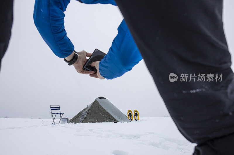 成熟的游客在冬季山地露营时使用手机，独自在大自然中。