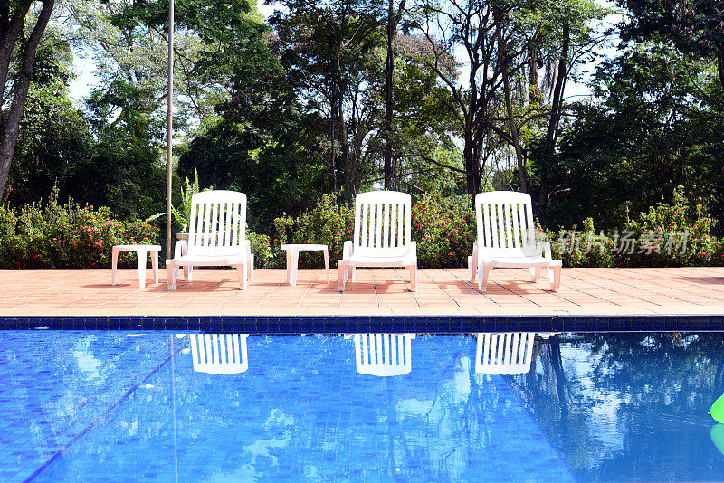 游泳池，白色的椅子和自然花园的背景