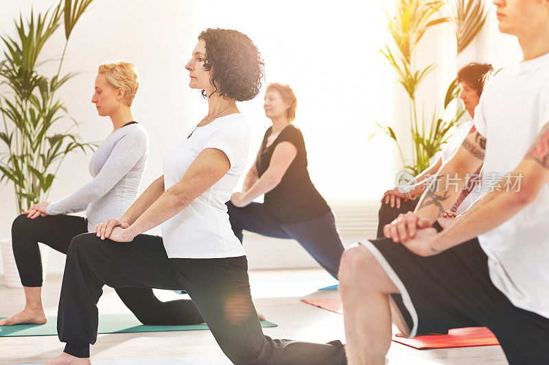 一间平静的瑜伽练习者伸展身体和冥想，以改善身体、心灵和精神的健康和健康。一群人在瑜伽课上做低弓步姿势