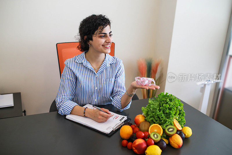 年轻漂亮的女营养师拿着卷尺，桌上放着健康的食物健康的饮食和减肥