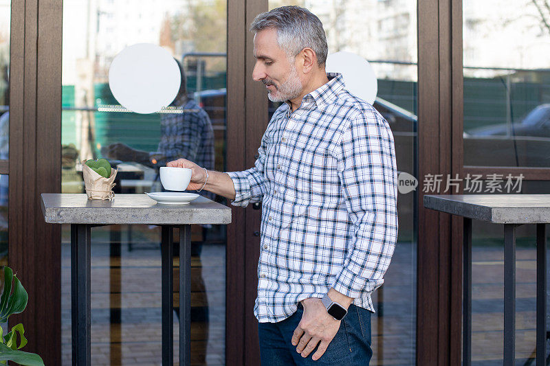 一个穿着格子衬衫的自信男子站在街边咖啡馆的桌子旁边