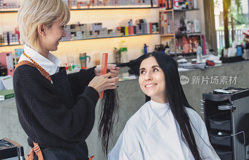 发型师用梳子和剪刀为女性客户理发。在美容美发沙龙的女人。美丽年轻的发型师在美容院为女顾客理发。