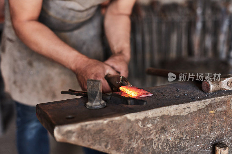 制造，金属和车间与一个人的铁匠工作在设计锻造创意产业。在铸造厂或工厂里，设计师、手和艺术与一名男性工匠一起在钢铁或铁上工作