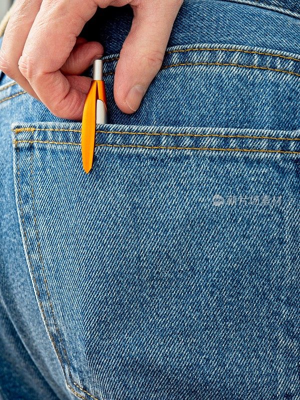 一名白人男子从蓝色牛仔裤的后口袋里掏出一支对比鲜明的橙色钢笔