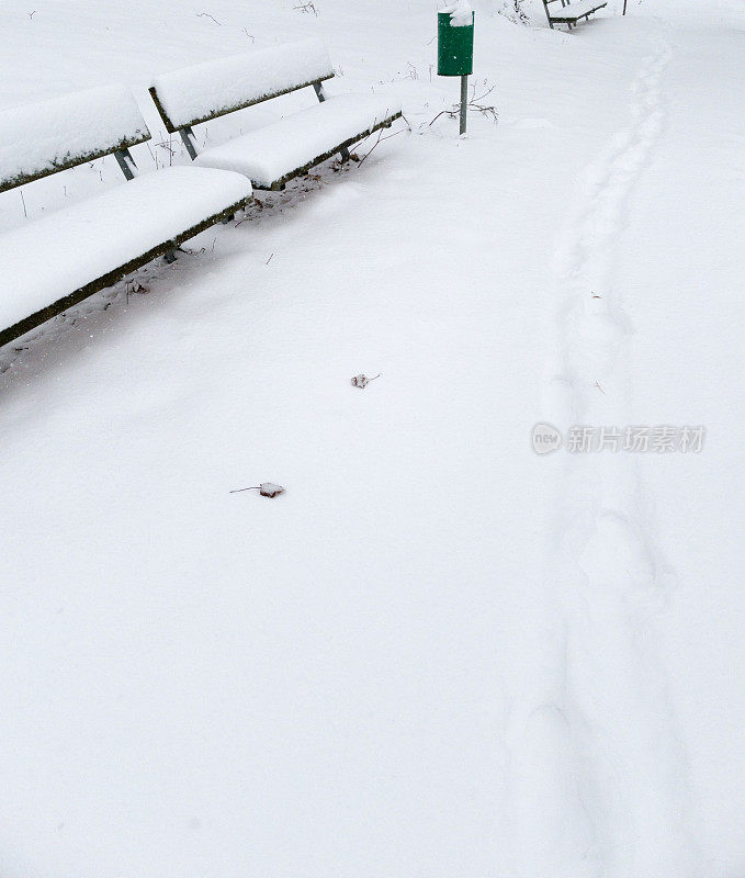 积雪覆盖的长凳旁的小路被踩在雪地里。