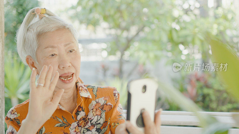 在户外使用智能手机视频通话的亚洲老年妇女，银发上网者，积极拥抱科技的老年妇女