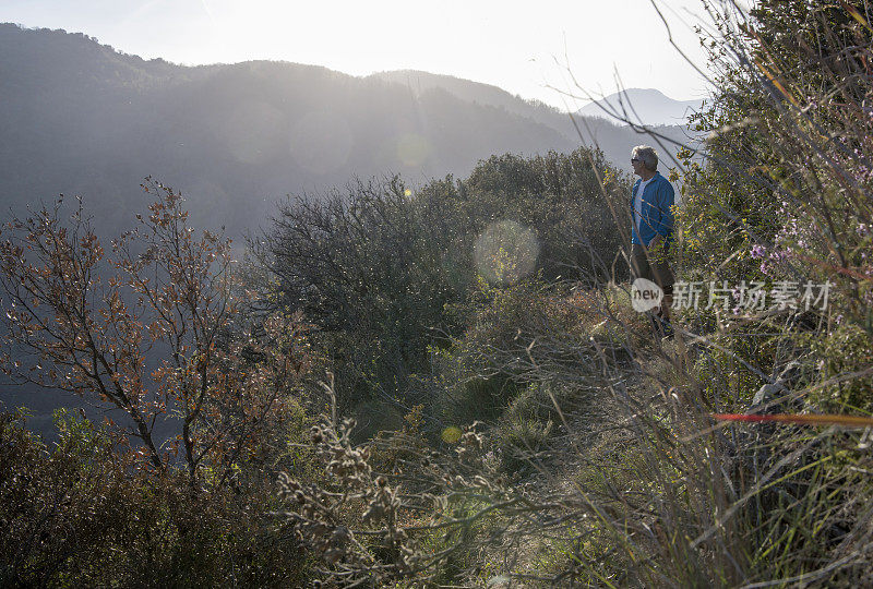 成熟的男性徒步旅行者走在狭窄的山路在丘陵设置