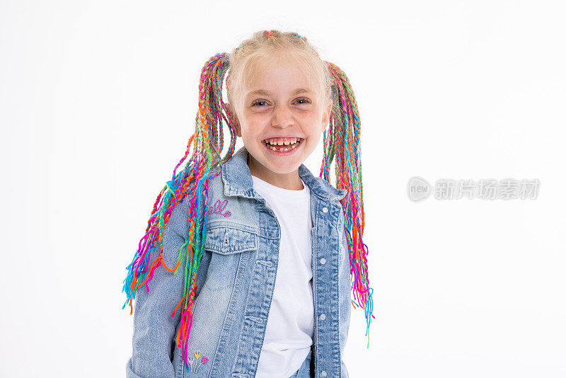 金发碧眼的女儿梳着彩色的辫子，穿着牛仔服装站在白色背景的摄影棚里对着镜头微笑