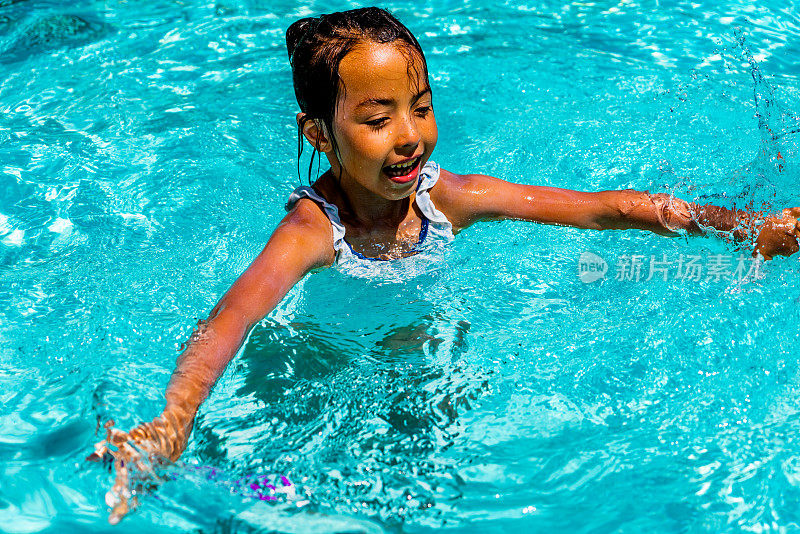 在一个温暖的夏日，一个7岁的小女孩兴高采烈地在游泳池里戏水玩耍，她的笑声回荡着，她高兴地抛起又捡起一根潜水棒。