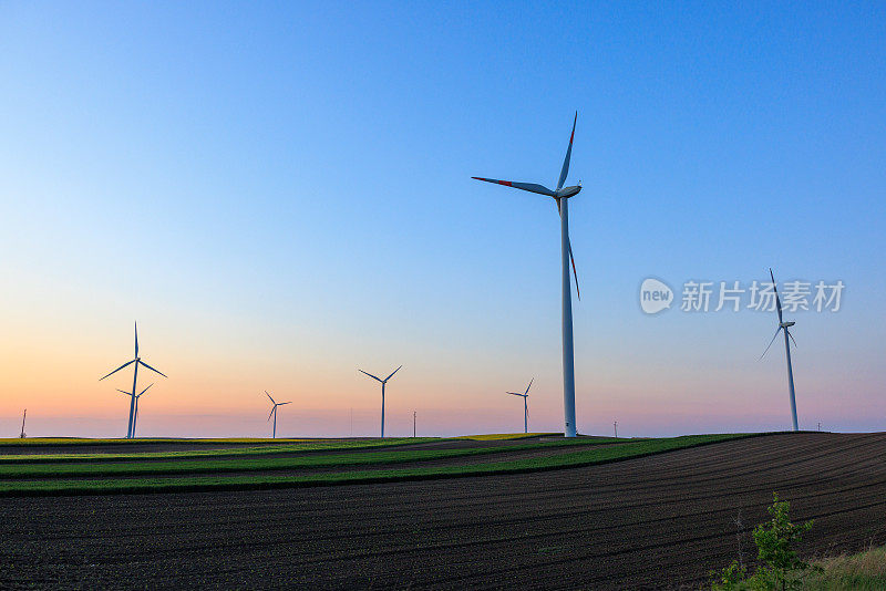 黄昏时分，蓝色和紫色的天空下，农田上的风力涡轮机农场