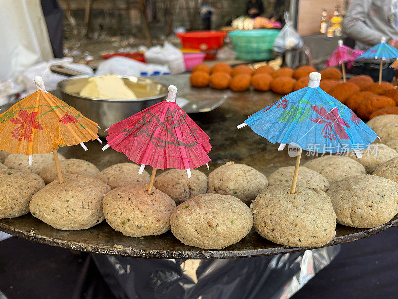 印度街头小吃摊Tawa(大而平的金属锅)的特写图像，金属碗的黄油和金属刮刀，准备煎鹰嘴豆饼，鸡尾酒伞，重点在前景