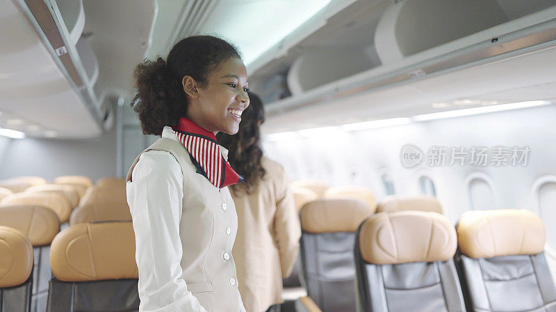 身着制服的迷人非裔美国女空姐微笑地站在飞机的经济舱里。女乘务员在飞机上向乘客打招呼。航空公司的概念